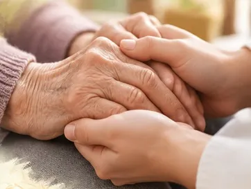 Des mains jeunes posées avec douceur sur les mains d’une personne âgée.